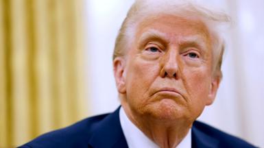 A close up headshot of US President Donald Trump looking on as reporters ask questions, after he signed a series of executive orders in the Oval Office of the White House on 23 January