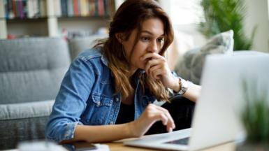 Young woman with brown hair, wearing a denim jacket, looking at a laptop screen