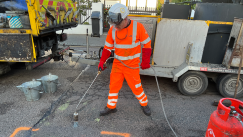 Pothole being repaired by a man in orange high visibility clothing