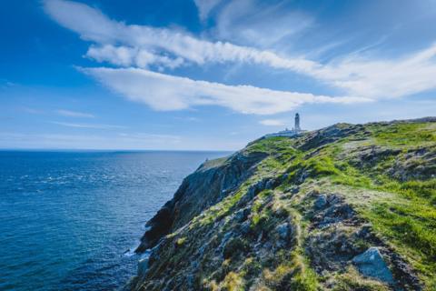 The Mull of Galloway lighthouse on a cliff edge with a beautiful blue sky overhead