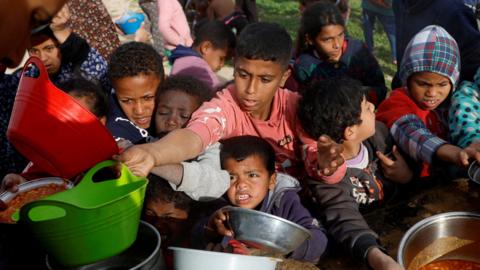 Palestinian children gather to receive food cooked by a charity kitchen, during the Muslim holy month of Ramadan, in Khan Younis, in the southern Gaza Strip, 3 March 2025.