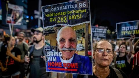 A woman holds up a placard with a picture of Shlomo Mantzur on it 