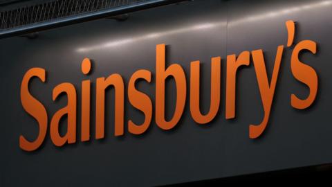 An orange Sainsbury's sign on a black wall.