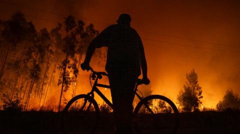 silhouette of a man on a bike with forest fire in background