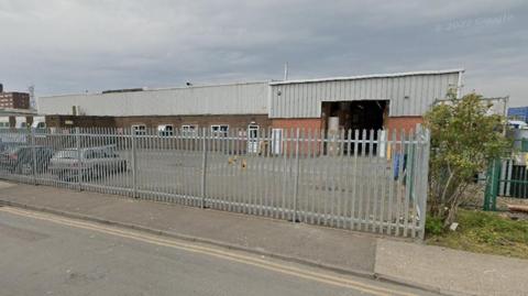 The current recycling centre warehouses clad in grey sheeting and surrounded by a high metal grey fence 

