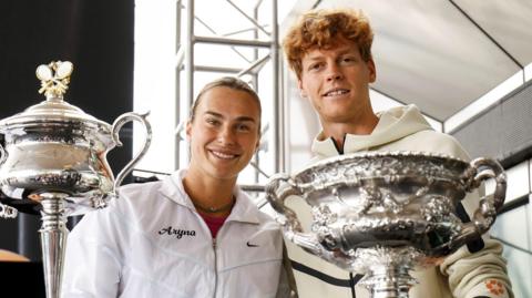 Aryna Sabalenka and Jannik Sinner pose with the Australian Open trophies at Melbourne Park