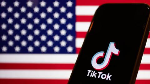 TikTok logo is displayed on the screen of an iPhone with an American flag background.