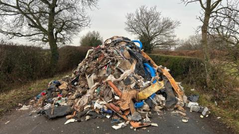 A huge pile of illegally dumped waste material which appears to include housebuilding materials and tubing and various other items.