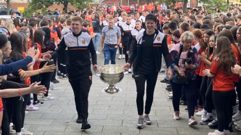 Armagh players hold Sam Maguire cup as they parade through a group of pupils towards their old school