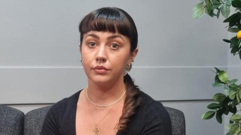 Catherine McSherry , a woman with long brown hair pulled back behind her neck, she has a black top and a gold necklace and earrings