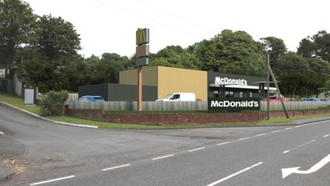 A computer generated view of a McDonald's restaurant next to the A77 road in southern Scotland with trees in the background and cars using the drive through