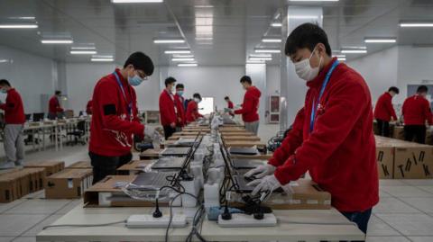 File picture showing workers in red tops and wearing face masks preparing laptops ahead of the Beijing 2022 Winter Olympics