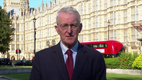 Hilary Benn stands in front of the houses of parliament in a suit talking to the BBC remotely  