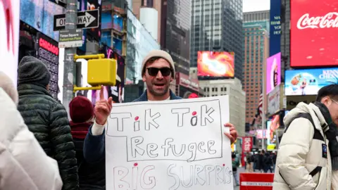 A man holding a sign saying he is a TikTok refugee, while he stands in New York's Times Square