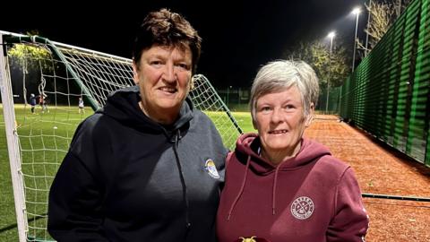 Colleen O'Connor and Mandy Beach on a floodlit astroturf football pitch.