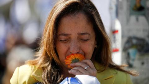 An Israeli woman kisses an orange flower while watching the funeral procession of Shiri, Ariel and Kfir Bibas (26 February 2025)