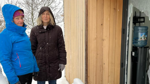 Two women standing outside a building with broken window in the snow 