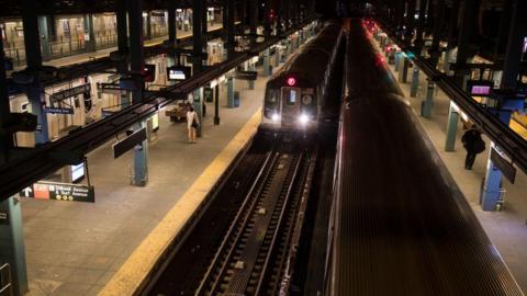 The F train subway line arrives at the concrete platform. 