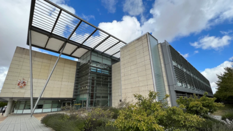 Exterior of South Cambs District Council offices taken from a low angle. It is  a modern three-storey pale brick building with iron struts.