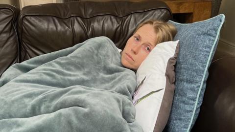 Becky Williams lies on sofa at home covered in a blanket