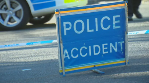 A blue sign on a road with the words 'Police Accident' in white letters.