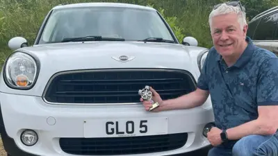 Neal Bircher poses on bent knee in front of his white Mini that has a 'GLO 5' number plate