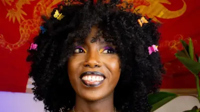 Gros plan sur la Youtubeuse Muthoni Gitau avec des papillons dans les cheveux.