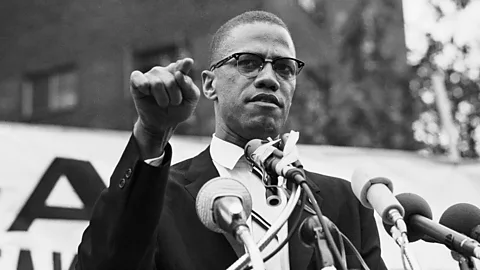 A black-and-white photo of Malcolm X speaking at a podium (Credit: Getty Images)