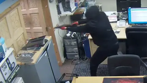 Masked man holding a sawn-off shotgun about to fire a shot inside the store