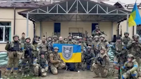 Reuters Ukrainian troops pose with flags in a village retaken from Russian control in the north-eastern Kharkiv region. Photo: 11 September 2022