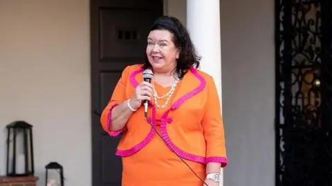 Getty Images British Ambassador to the US Dame Karen Pierce, clutching a microphone and wearing a bright orange dress and jacket with red trimming attends the BAFTA mentorship program launch with the British ambassador and Consul General on December 05, 2021 in Los Angeles, California