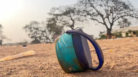 A green lunch pail lies on its side on a dusty field