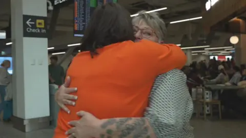 Two women hugging at an airport.