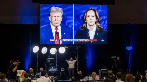 Donald Trump and Kamala Harris seen on a huge TV screen