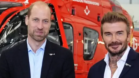 Prince William and David Beckham pose in front of a helicopter