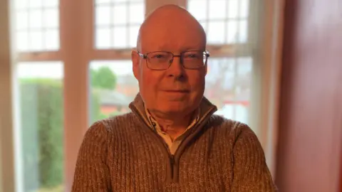 A bald man with glasses in a zip-top jumper