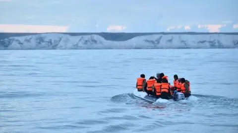 A small boat in water with a number of people wearing high-visibility jackets. The boat and the occupants are facing away from the camera. 