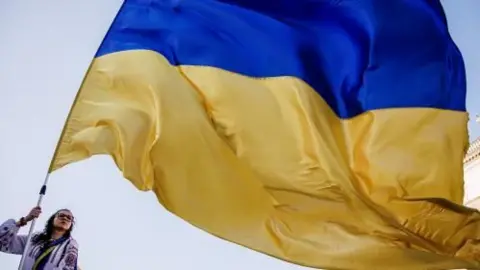 A woman wearing glasses waves a giant Ukrainian flag in blue and yellow colours