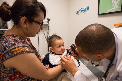 Pediatric Asthma. A doctor examines a child with asthma as the child's mother holds the child on her lap.