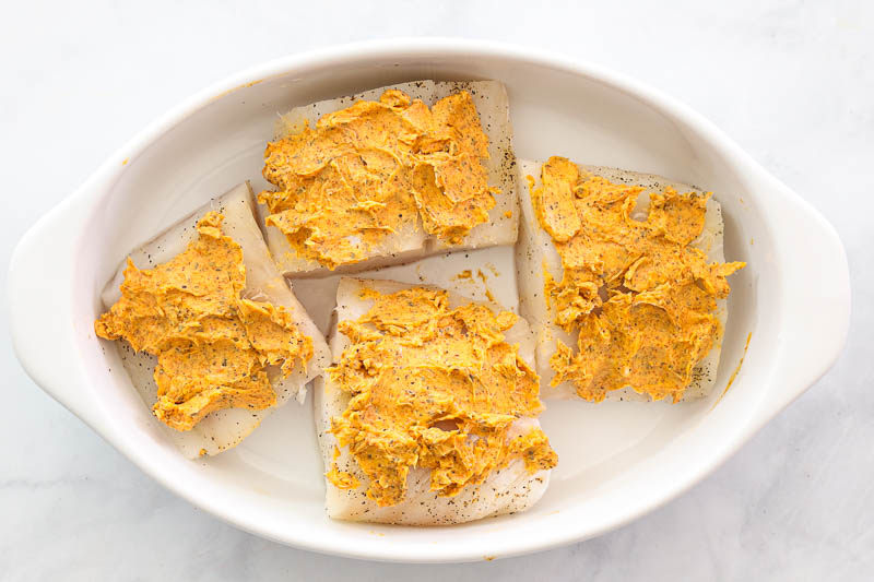 overhead image of buttered cod fillets in a white baking dish