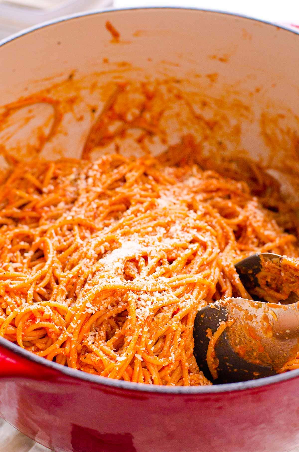 Spaghetti in tomato sauce with Parmesan cheese in a pot with metal tongs.