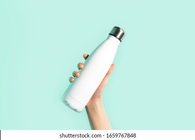 Close-up of female hand, holding white reusable steel stainless eco thermo water bottle with mockup, isolated on background of cyan, aqua menthe color. Be plastic free. Zero waste.