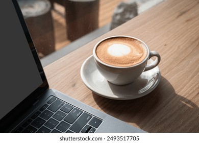 Close-up of Hot coffee latte with latte art milk foam in cup mug and laptop computer on wood desk office desk in coffee shop at the cafe,during business work concept