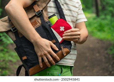 Close-up of a person taking a first aid kit out of a backpack while on a forest trail, highlighting outdoor preparedness and safety. 