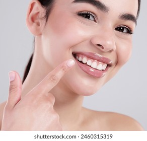 Happy woman, portrait and pointing with teeth for dental care, hygiene or treatment on a gray studio background. Closeup of young female person with big smile for tooth whitening, lip gloss or glow