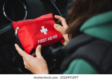 A person is carefully holding a bright red first aid kit securely inside a car, emphasizing the crucial importance of being prepared for emergencies while traveling on the road