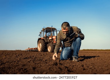 Portrait of satisfied mature farmer standing in field with tablet supervises the cultivation of soil.	