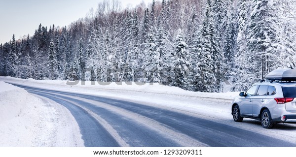 Suv car with rooftop cargo carrier trunk stay\
on roadside of winter road. Family trip to ski resort. Winter\
holidays adventure. car on winter\
road