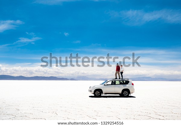 Tourists on white car rooftop in spacious sunshine\
Salar de Uyuni