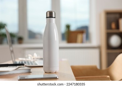 White thermos bottle at wooden table indoors